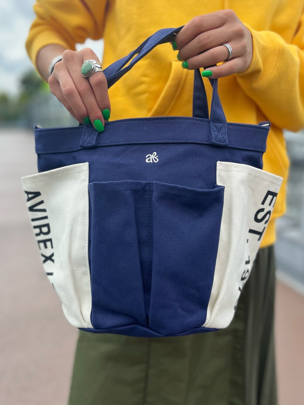 イエロー系のパーカー、ブルー系のトートバッグ、グリーン系のスカートを着用したレディースの秋コーディネートの4枚目の写真