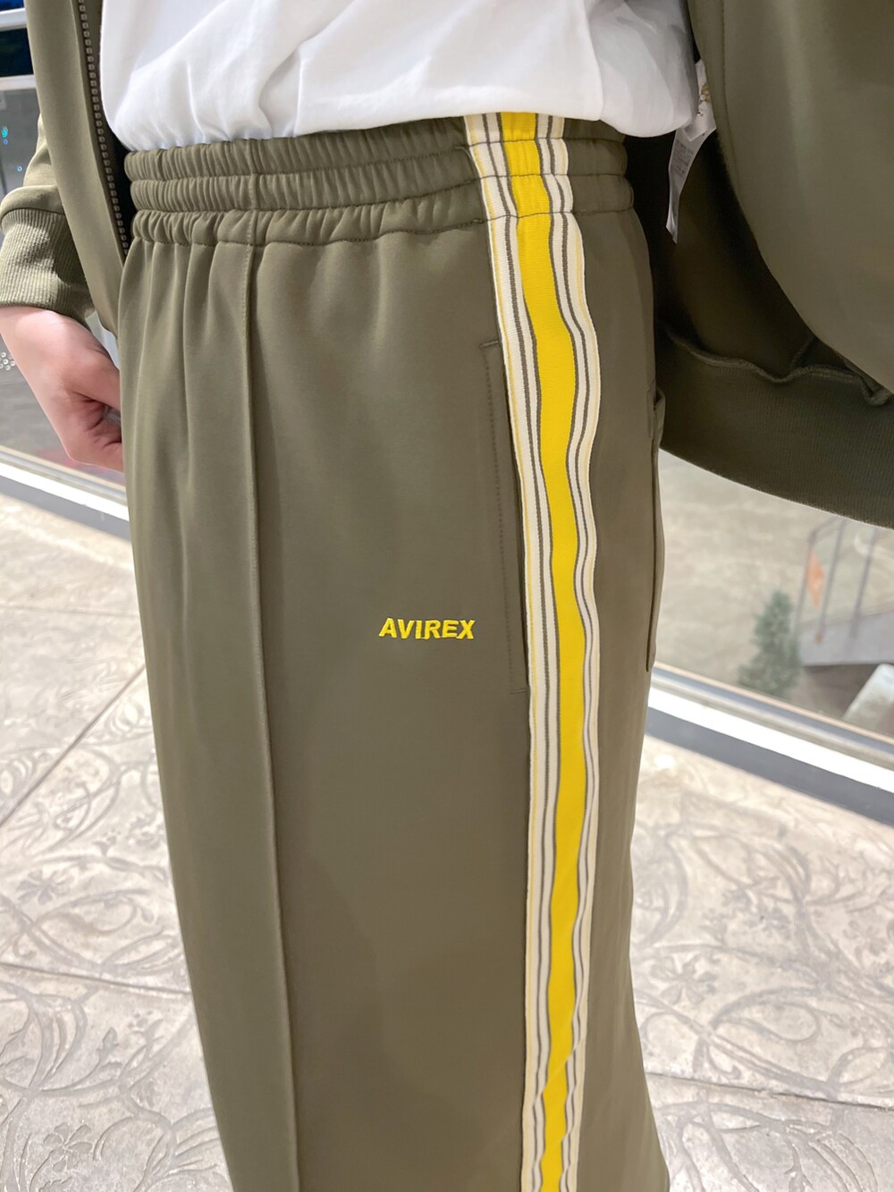 グリーン系のジャージ、グリーン系のスカート、オレンジ系のTシャツ/カットソーを着用したレディースの春コーディネートの3枚目の写真