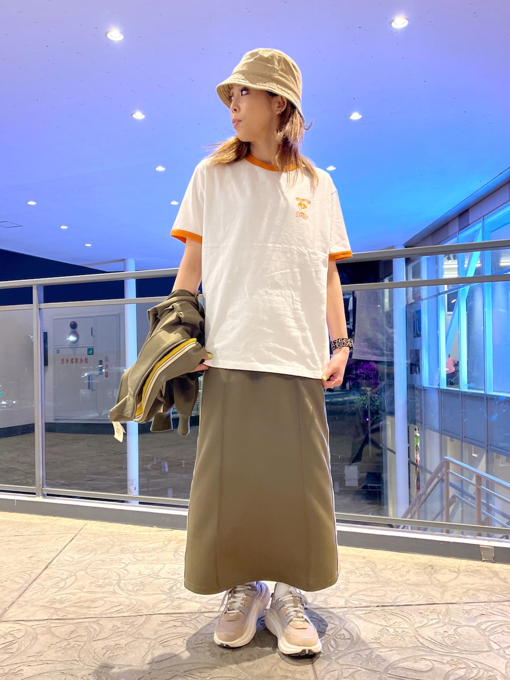 オレンジ系のTシャツ/カットソー、グリーン系のスカート、グリーン系のジャージを着用したレディースの春コーディネートの2枚目の写真