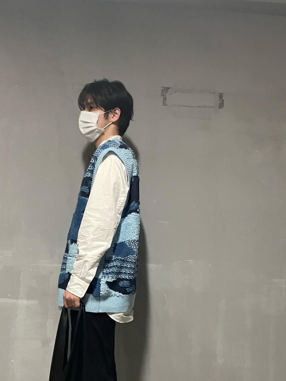 ブラック系のスラックス、ベージュ系のトートバッグ、ブルー系のベストを着用したメンズの春コーディネートの2枚目の写真