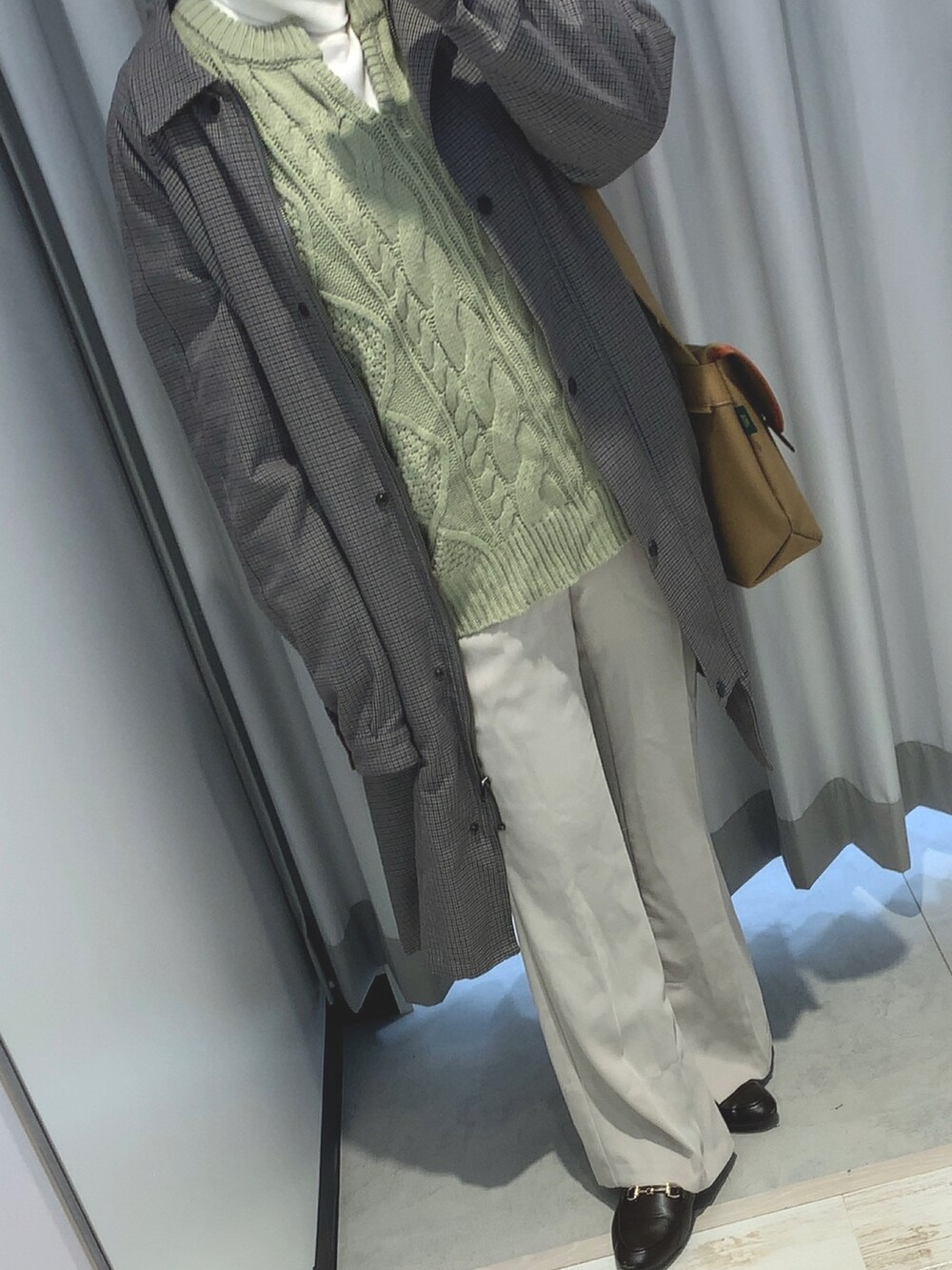 グレー系のステンカラーコート、ブラウン系のローファー、グリーン系のニット/セーターを着用したレディースの冬コーディネートの2枚目の写真