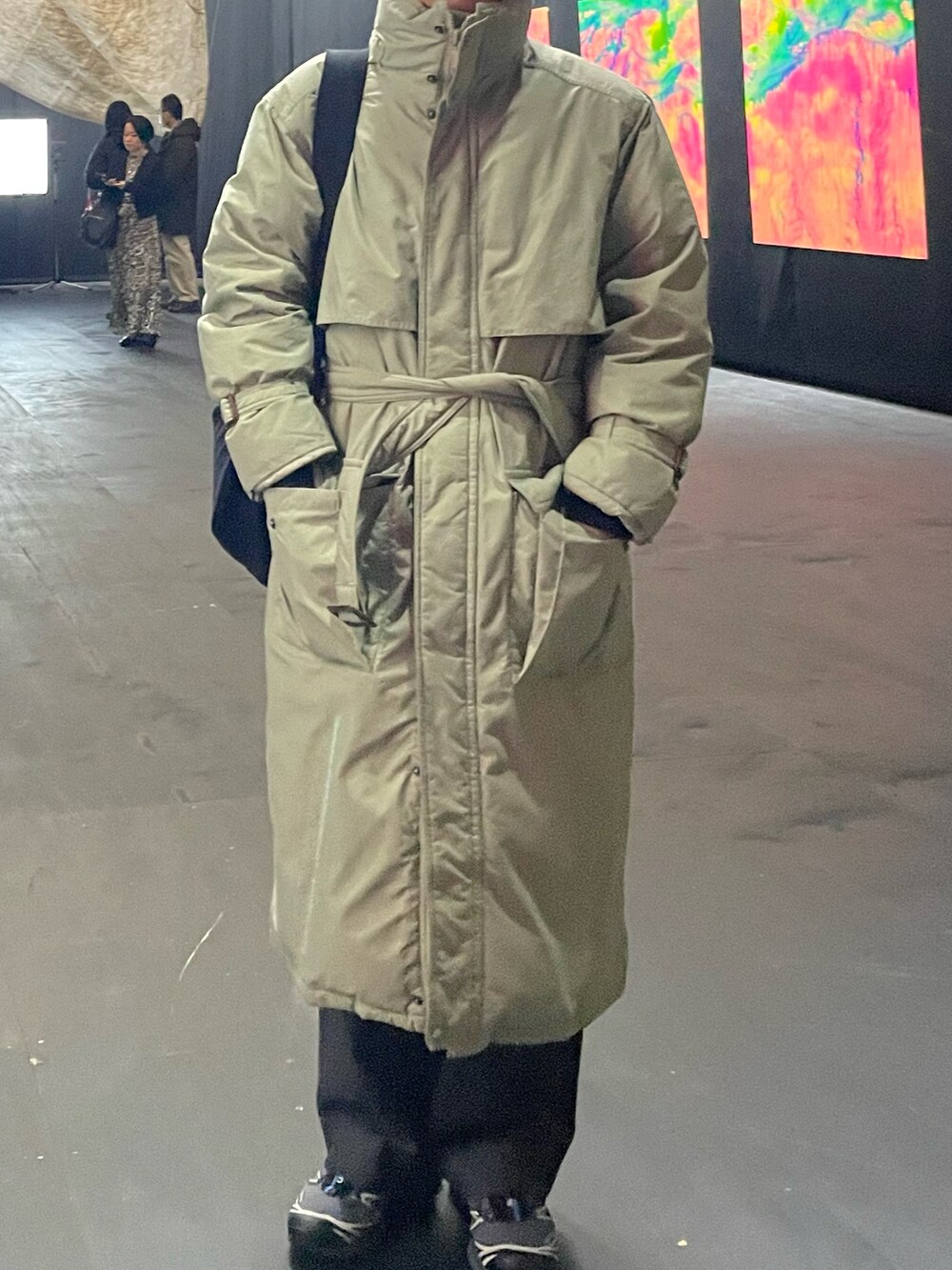 ブラック系のバッグ、グレー系のスラックス、ブルー系のスニーカーを着用したメンズの冬コーディネートの2枚目の写真