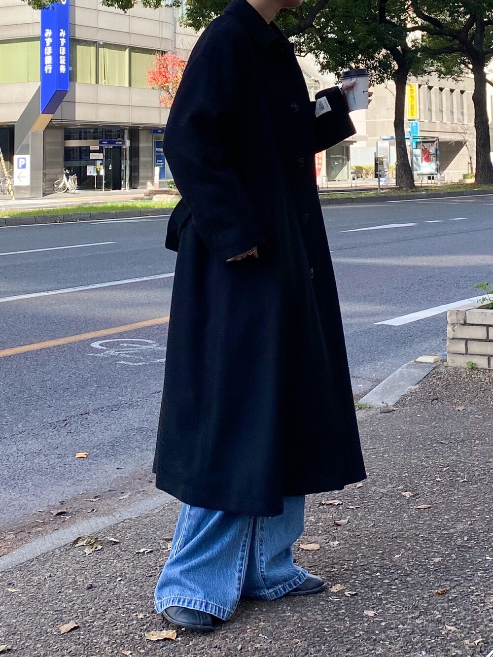 ブラック系のステンカラーコート、ブルー系のデニムパンツ、ピンク系のニット/セーターを着用したレディースの秋コーディネートの2枚目の写真