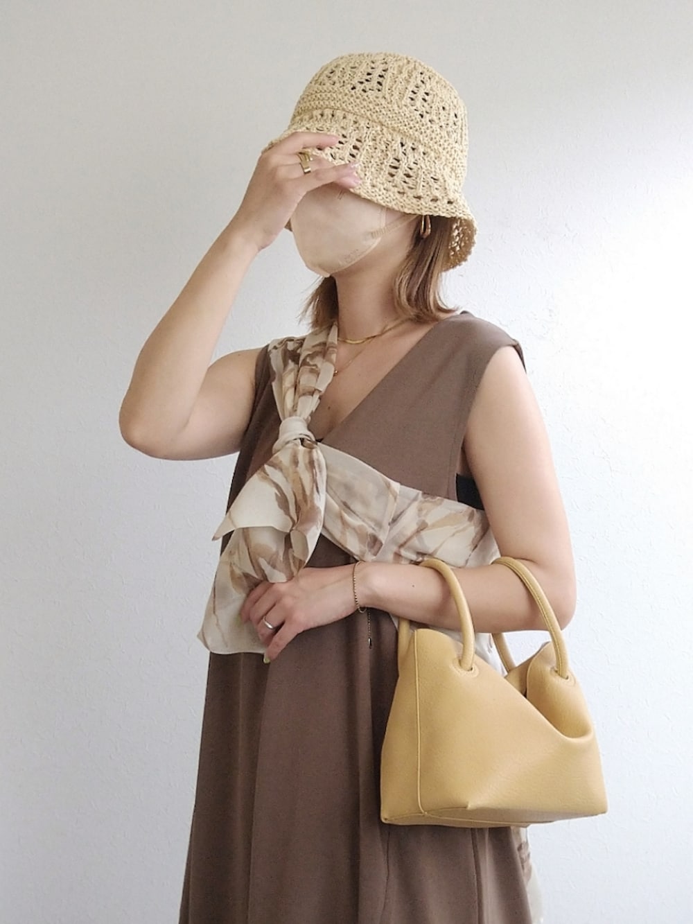 ブラウン系のジャンパースカート、イエロー系のハンドバッグ、ホワイト系のサンダルを着用したレディースの夏コーディネートの2枚目の写真