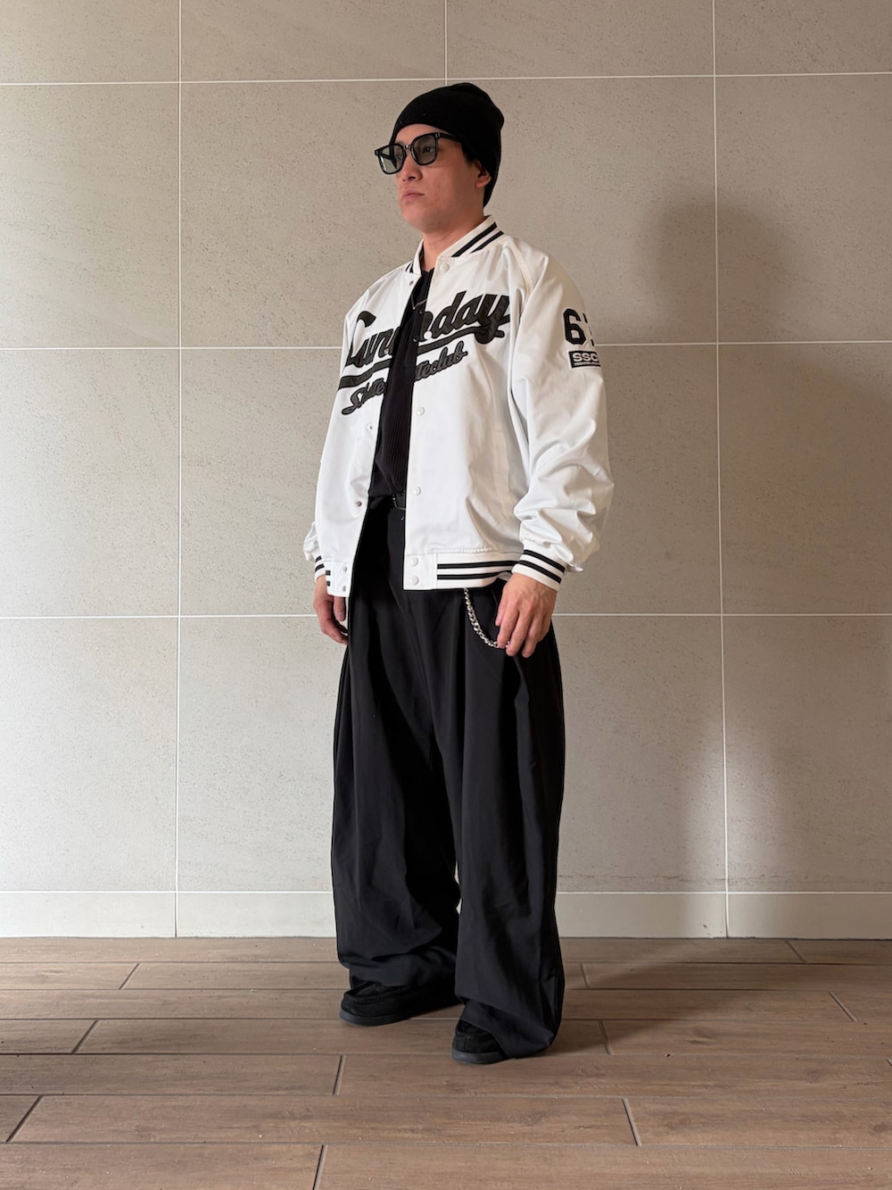 ブラック系のスラックス、ブラック系のモカシン/デッキシューズ、ホワイト系のスタジャンを着用したメンズの春コーディネートの2枚目の写真