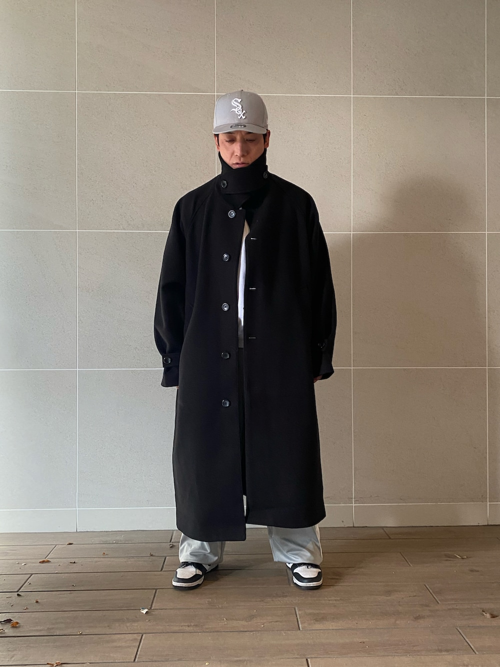 ブラック系のステンカラーコート、ホワイト系のスウェット、グレー系のその他パンツを着用したメンズの冬コーディネートの2枚目の写真