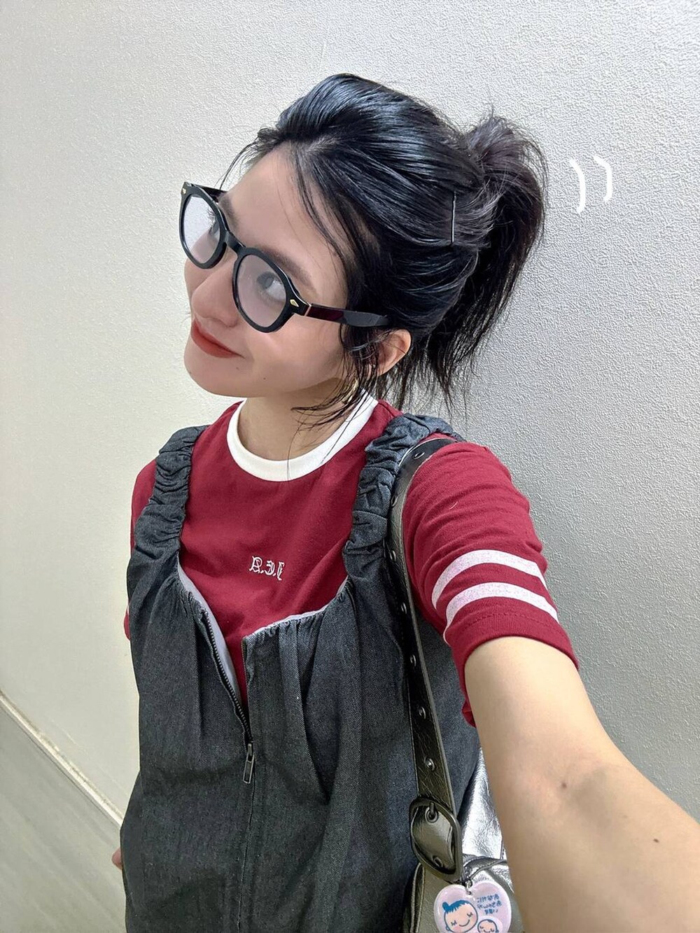 シルバー系のショルダーバッグ、レッド系のTシャツ/カットソー、グレー系のジャンパースカートを着用したレディースの夏コーディネートの3枚目の写真