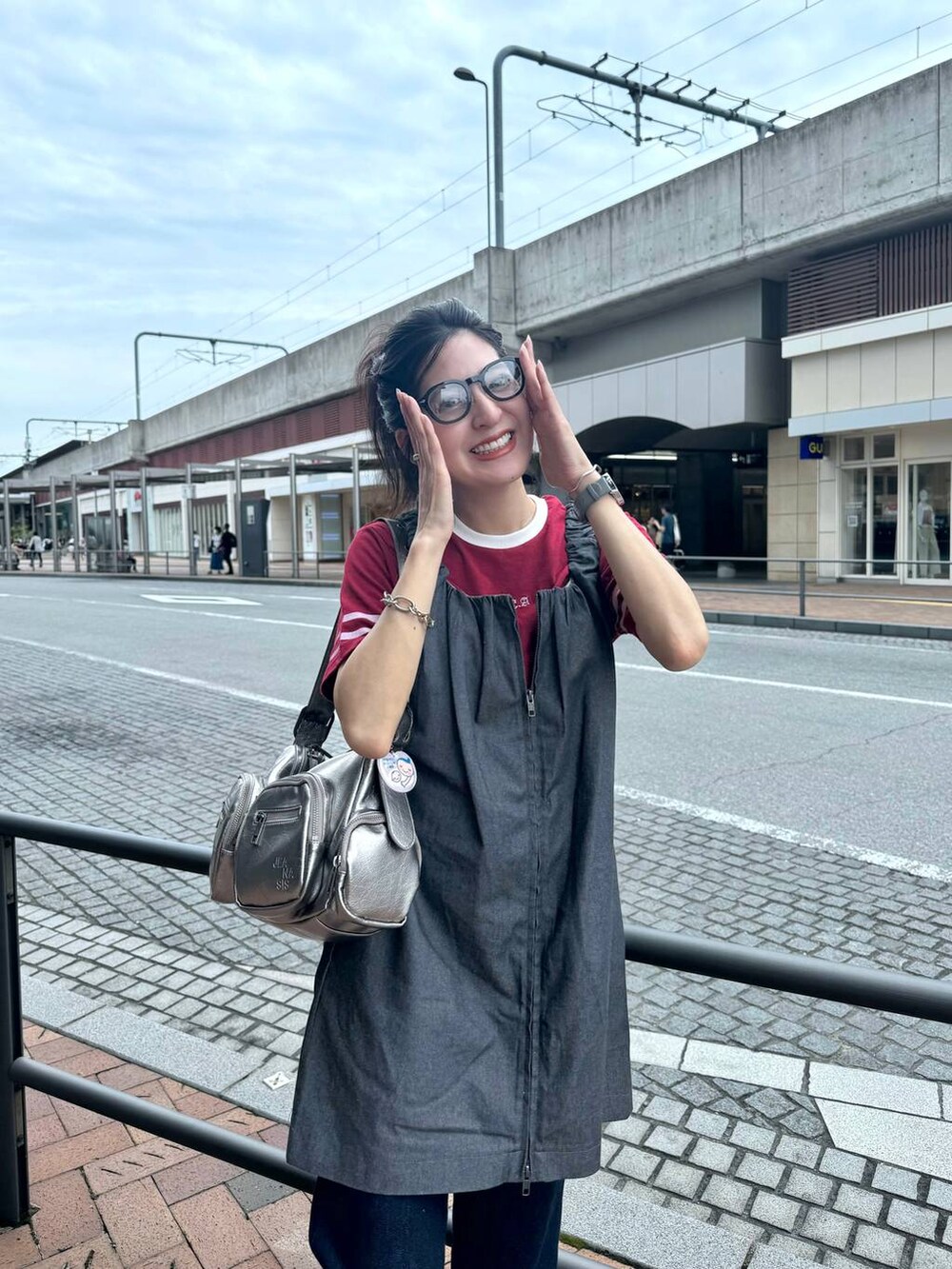 シルバー系のショルダーバッグ、レッド系のTシャツ/カットソー、グレー系のジャンパースカートを着用したレディースの夏コーディネートの5枚目の写真