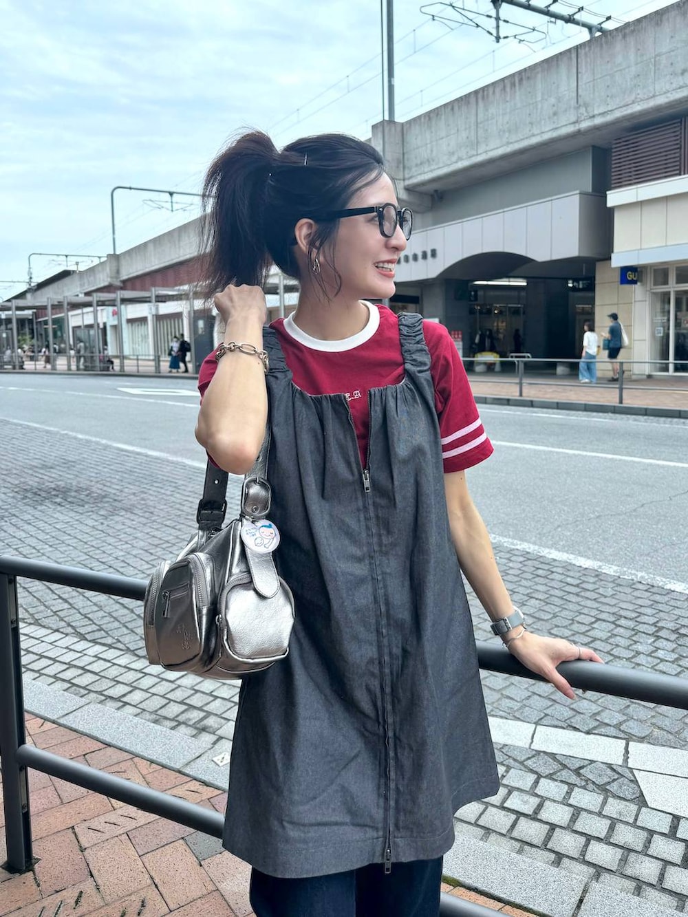 シルバー系のショルダーバッグ、レッド系のTシャツ/カットソー、グレー系のジャンパースカートを着用したレディースの夏コーディネートの4枚目の写真