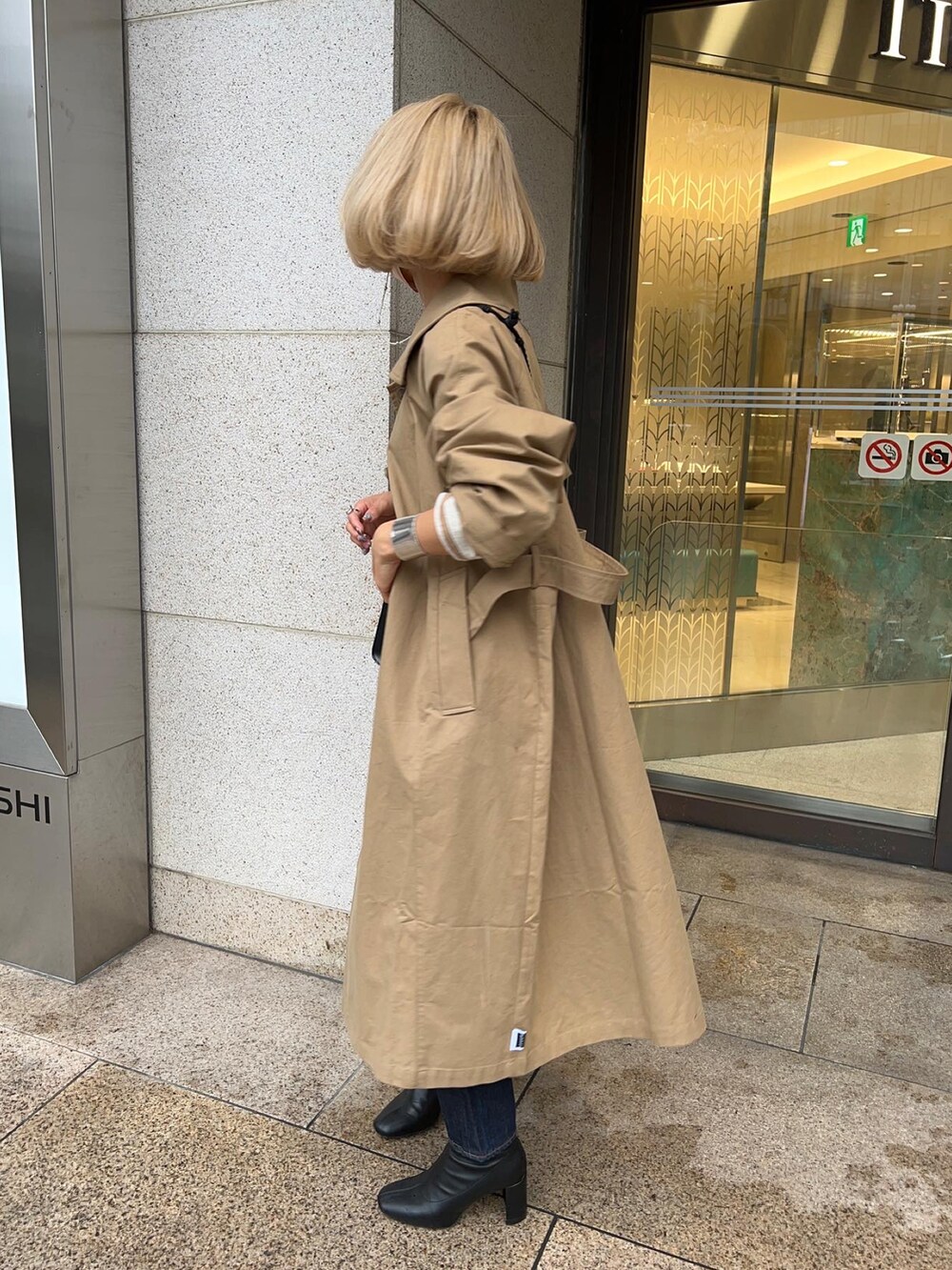 ベージュ系のトレンチコート、ブラック系のブーツ、ブルー系のデニムパンツを着用したレディースの春コーディネートの2枚目の写真