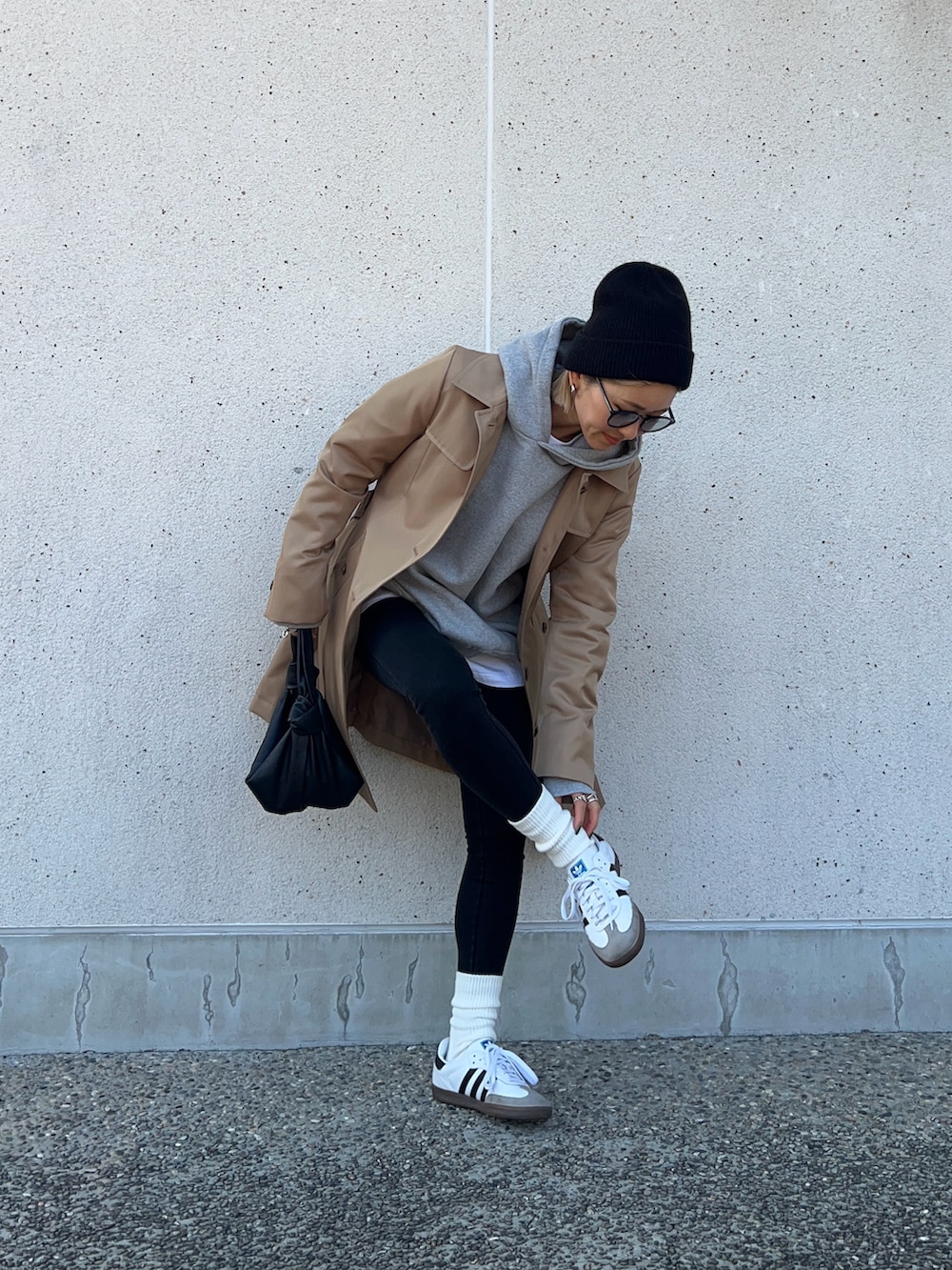 ベージュ系のトレンチコート、ブラック系のバッグ、ホワイト系のスニーカーを着用したレディースの冬コーディネートの2枚目の写真