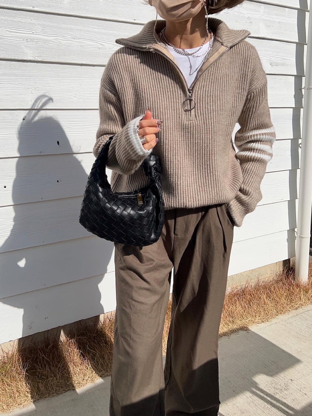 ホワイト系のスニーカー、ブラック系のハンドバッグ、ベージュ系のニット/セーターを着用したレディースの冬コーディネートの2枚目の写真