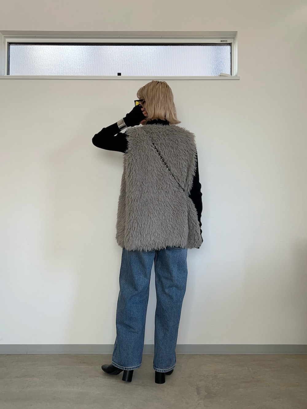 グレー系のベスト、ブルー系のデニムパンツ、ブラック系のブーツを着用したレディースの冬コーディネートの2枚目の写真