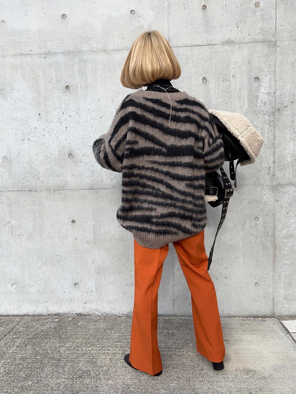 オレンジ系のスラックス、ブラック系のブーツ、グレー系のニット/セーターを着用したレディースの冬コーディネートの2枚目の写真