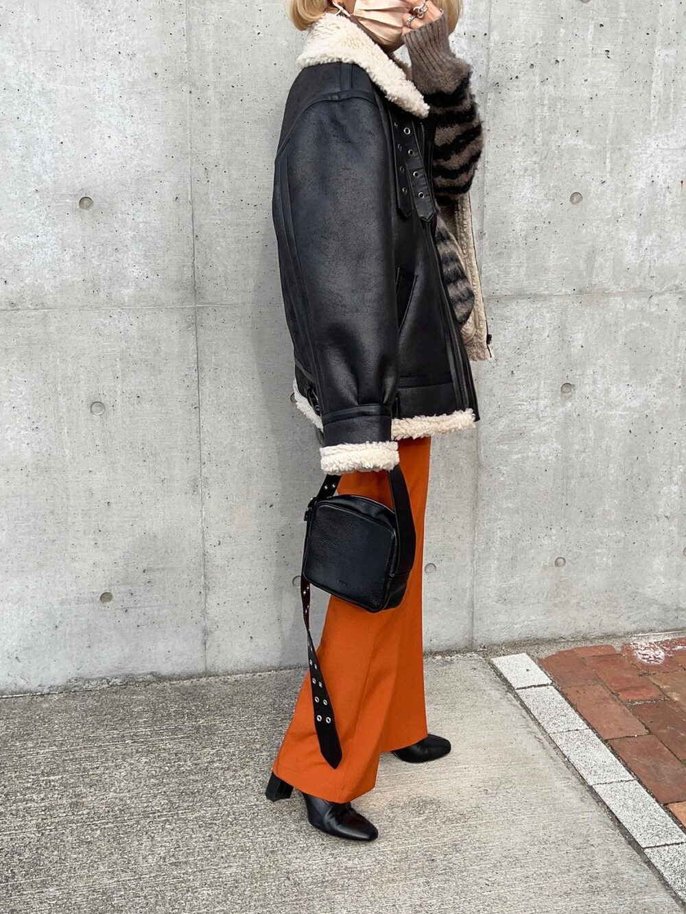 オレンジ系のスラックス、ブラック系のブーツ、グレー系のニット/セーターを着用したレディースの冬コーディネートの4枚目の写真