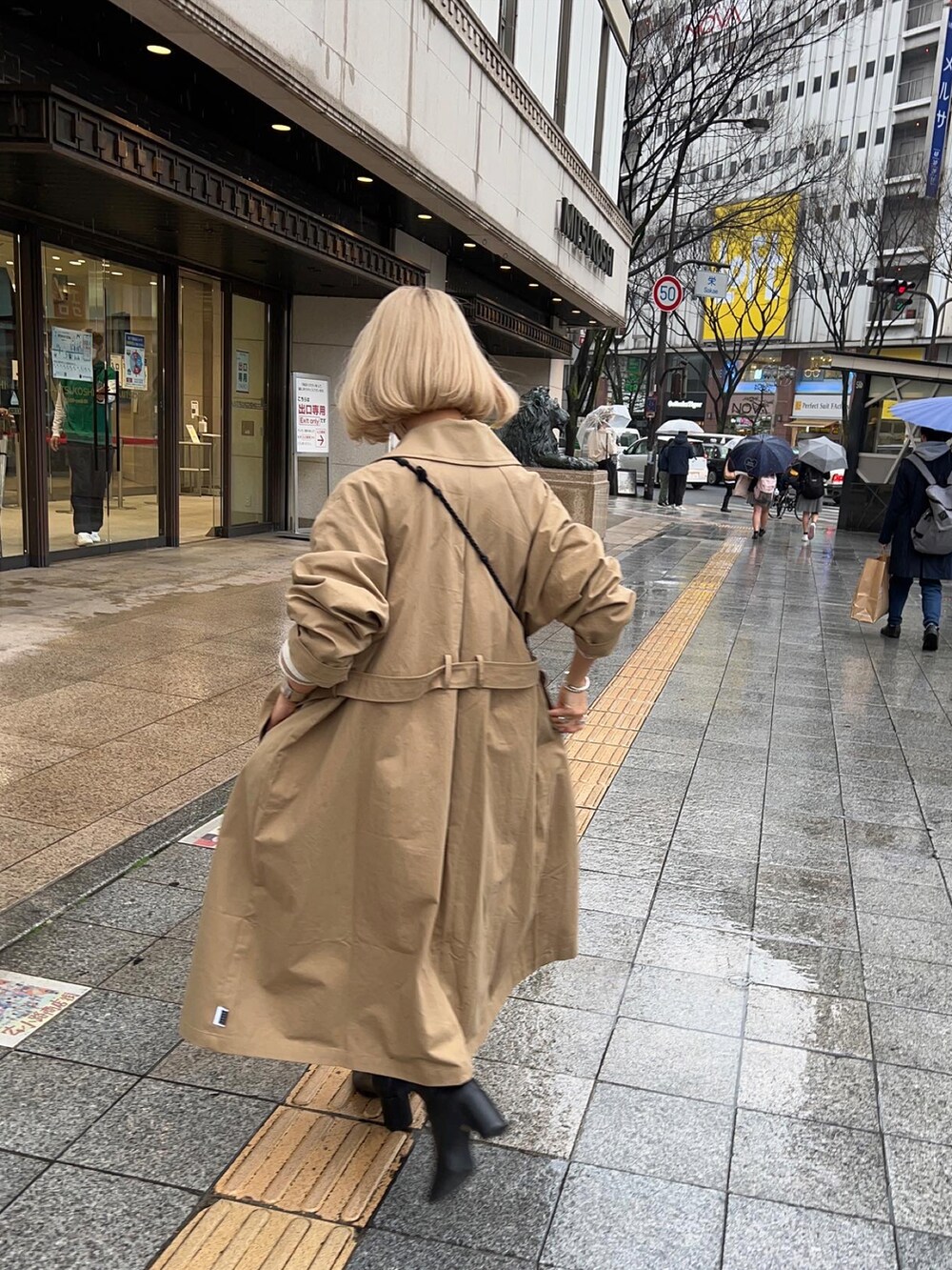 ベージュ系のトレンチコート、ブラック系のブーツ、ブルー系のデニムパンツを着用したレディースの春コーディネートの3枚目の写真