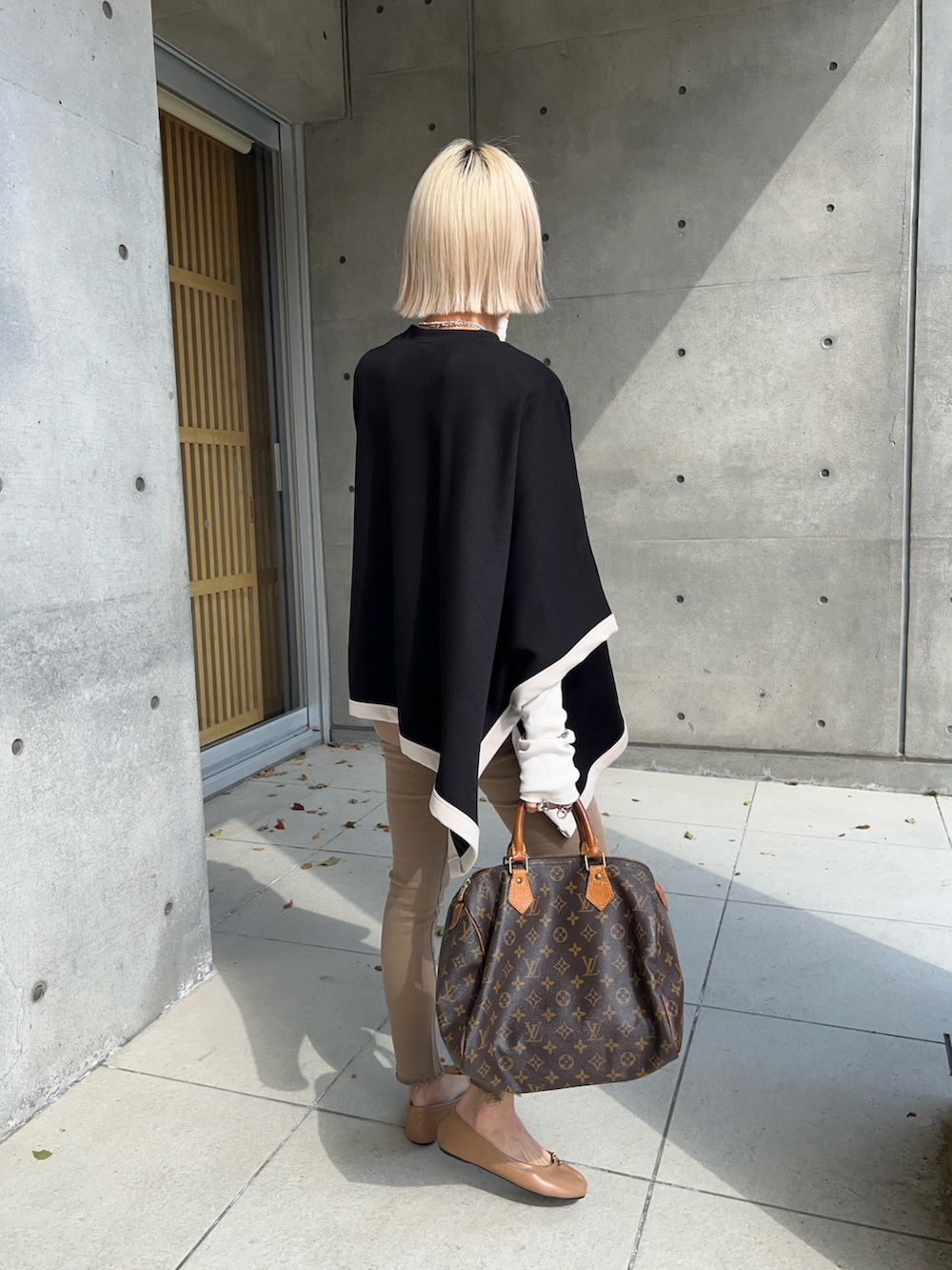 ブラック系のポンチョ、ホワイト系のTシャツ/カットソー、ベージュ系のパンプスを着用したレディースの春コーディネートの3枚目の写真