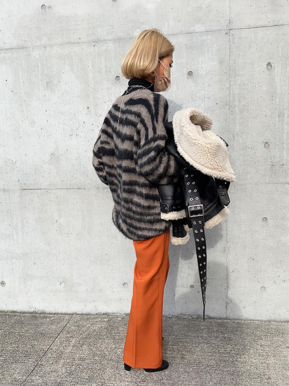 オレンジ系のスラックス、ブラック系のブーツ、グレー系のニット/セーターを着用したレディースの冬コーディネートの3枚目の写真