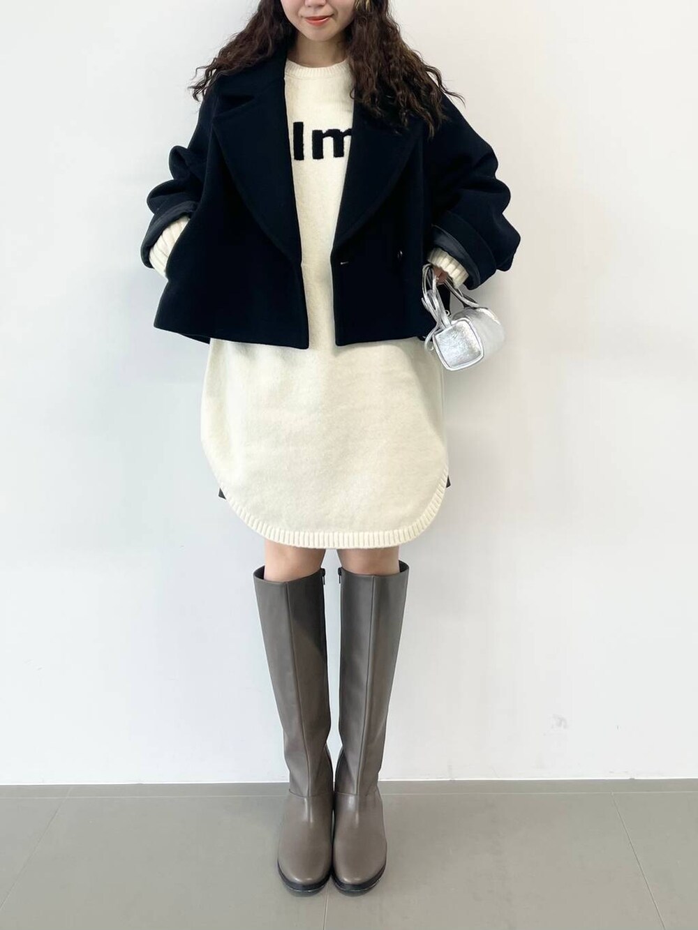 シルバー系のショルダーバッグ、ブラック系のピーコート、ホワイト系のワンピースを着用したレディースの冬コーディネートの5枚目の写真