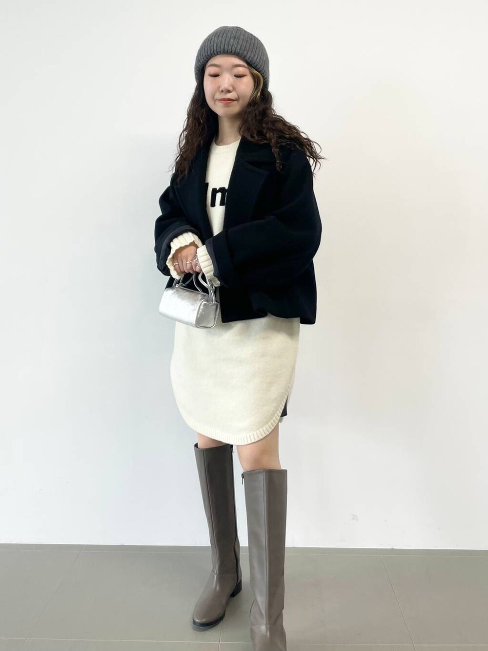 シルバー系のショルダーバッグ、ブラック系のピーコート、ホワイト系のワンピースを着用したレディースの冬コーディネートの2枚目の写真