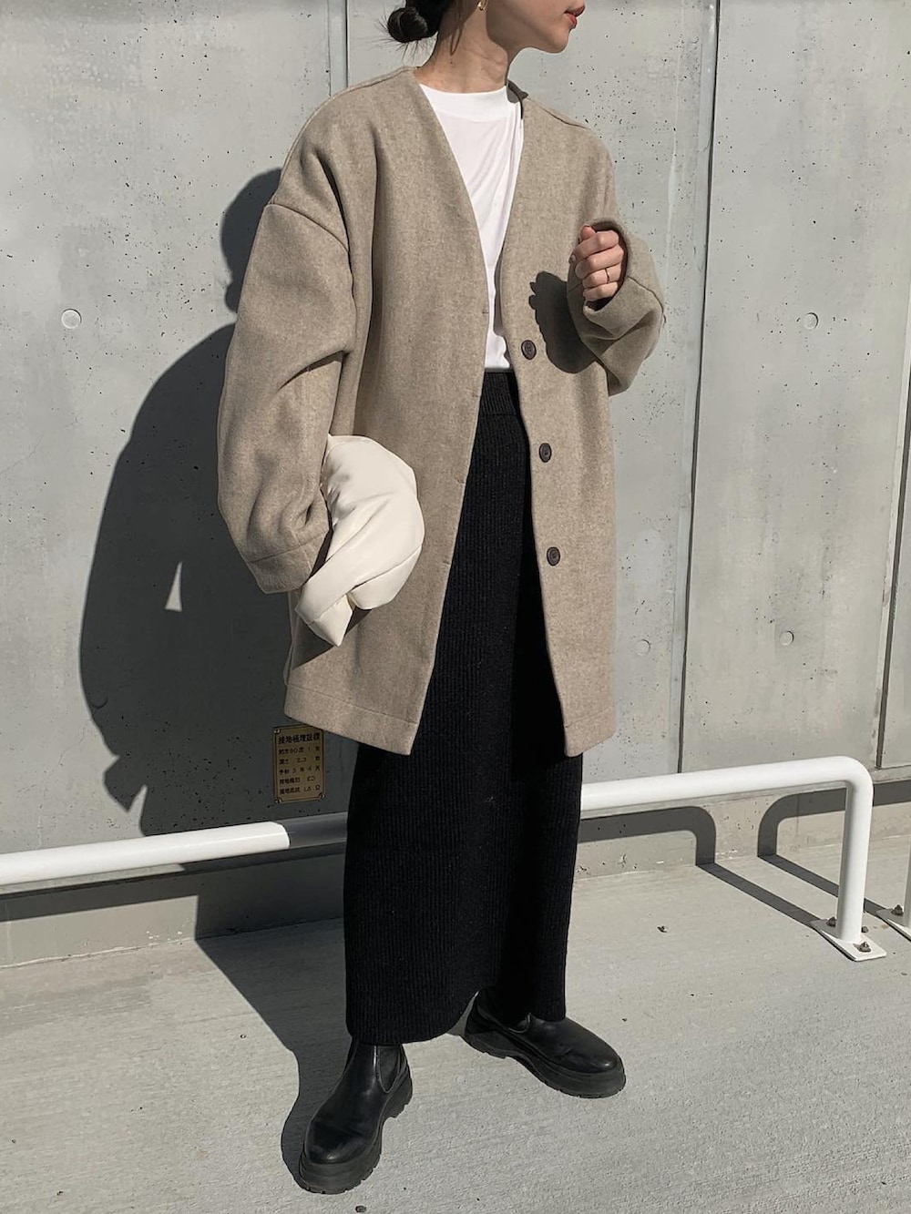 ベージュ系のノーカラーコート、ホワイト系のTシャツ/カットソー、ブラック系のセットアップを着用したレディースの冬コーディネートの2枚目の写真