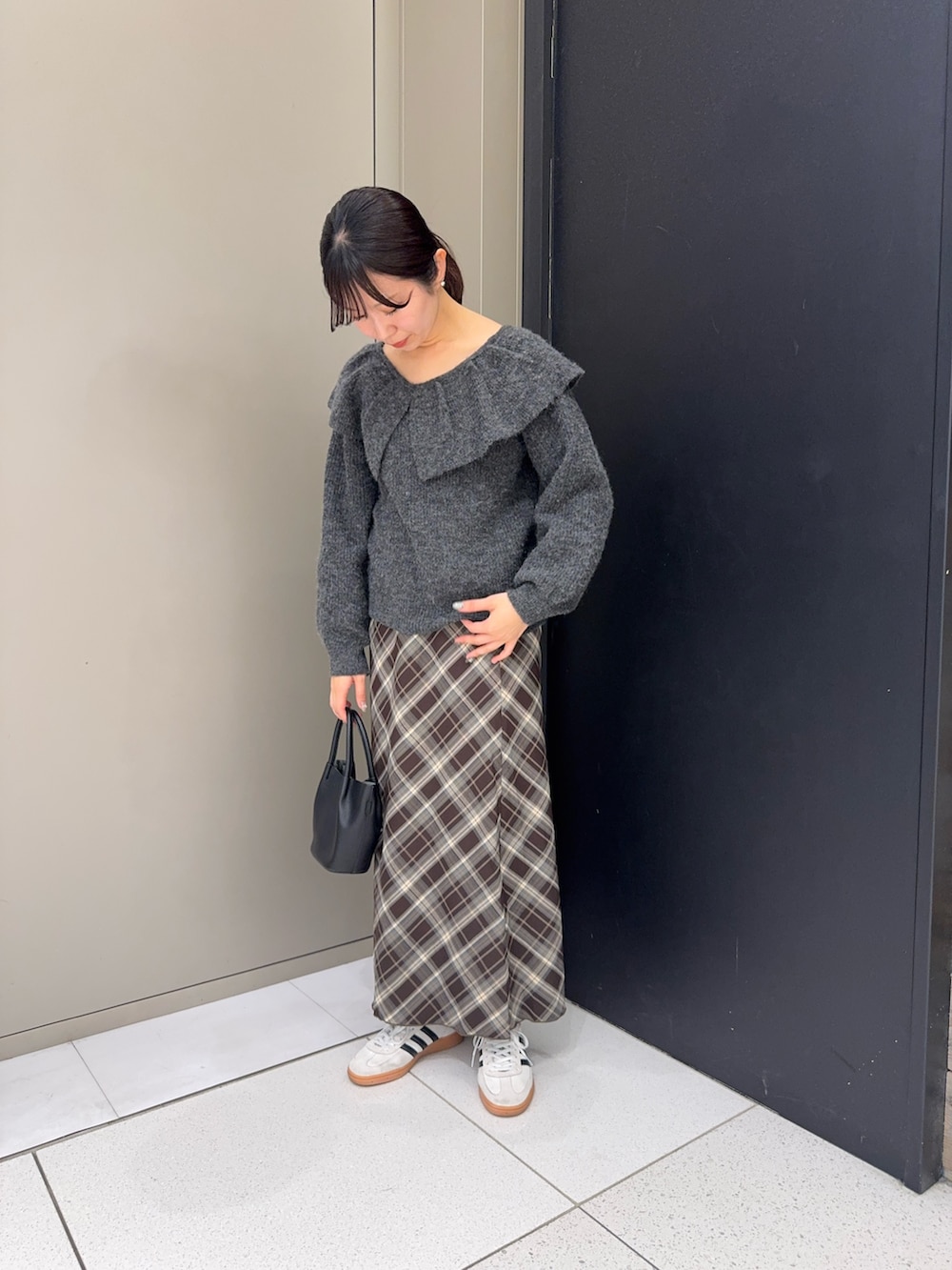 グレー系のニット/セーター、ブラック系のハンドバッグ、ブラウン系のスカートを着用したレディースの冬コーディネートの2枚目の写真