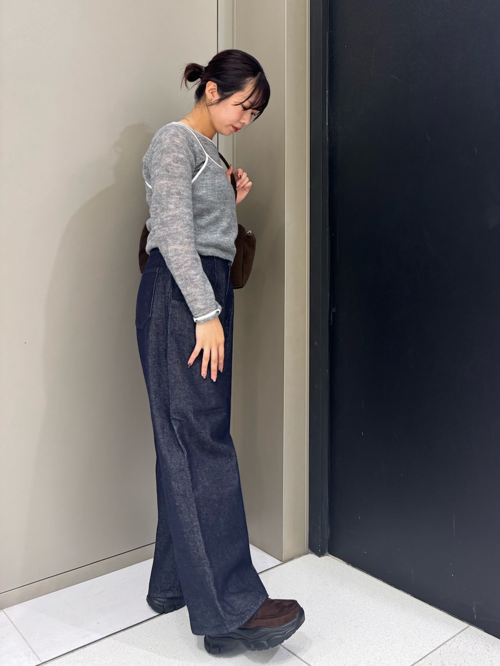 グレー系のニット/セーター、ブラウン系のボストンバッグ、ブルー系のデニムパンツを着用したレディースの秋コーディネートの3枚目の写真