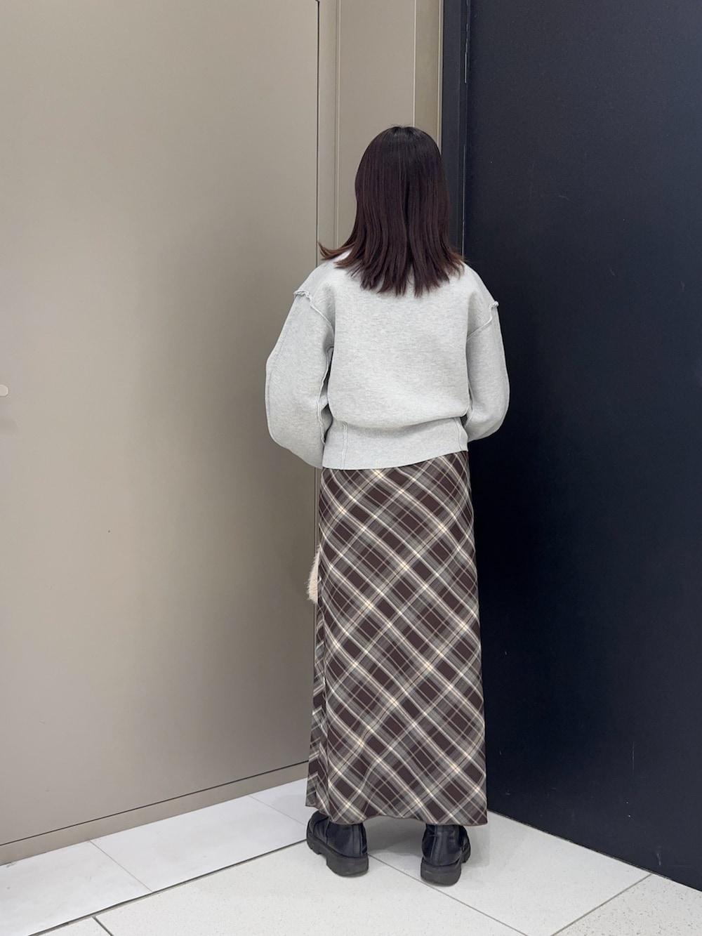 グレー系のニット/セーター、ブラウン系のスカート、ホワイト系のハンドバッグを着用したレディースの冬コーディネートの2枚目の写真