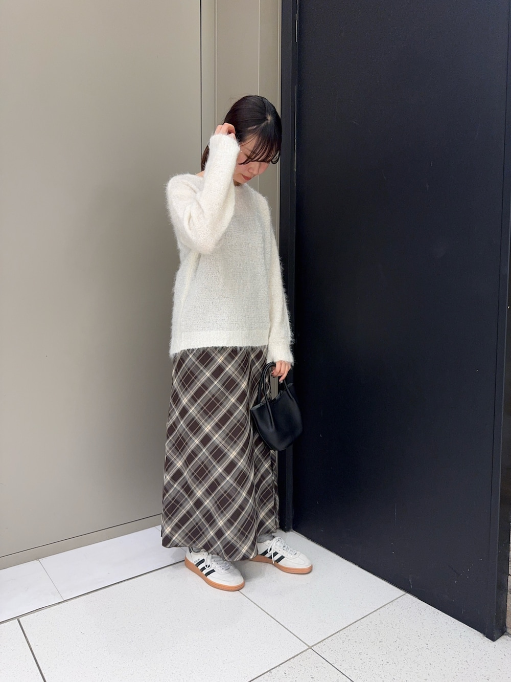 ブラック系のハンドバッグ、ブラウン系のスカート、ホワイト系のニット/セーターを着用したレディースの冬コーディネートの2枚目の写真