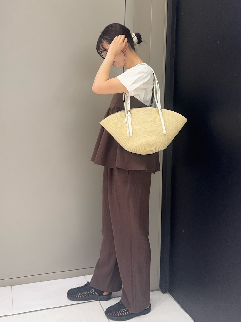 ブラック系のサンダル、ブラウン系のパンツ、ベージュ系のかごバッグを着用したレディースの夏コーディネートの2枚目の写真
