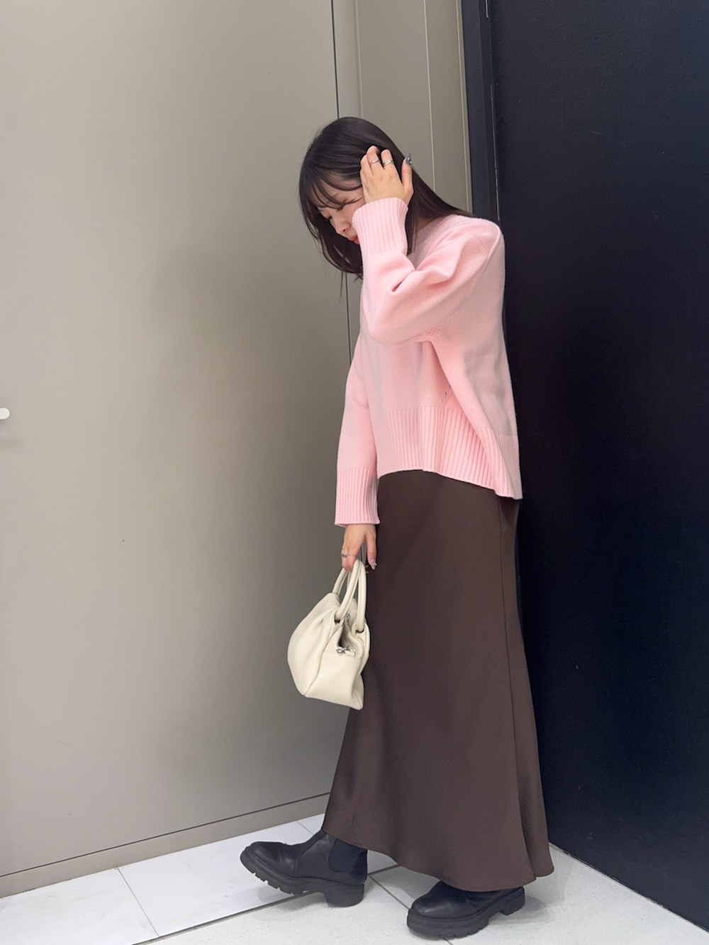 ブラウン系のスカート、ピンク系のニット/セーター、ホワイト系のハンドバッグを着用したレディースの冬コーディネートの2枚目の写真