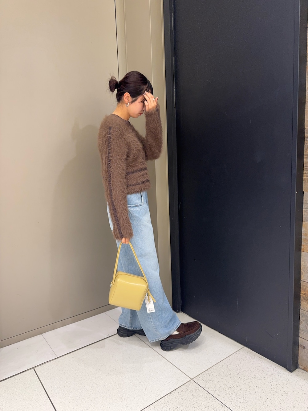 ブラウン系のニット/セーター、ベージュ系のショルダーバッグ、ブルー系のデニムパンツを着用したレディースの冬コーディネートの2枚目の写真