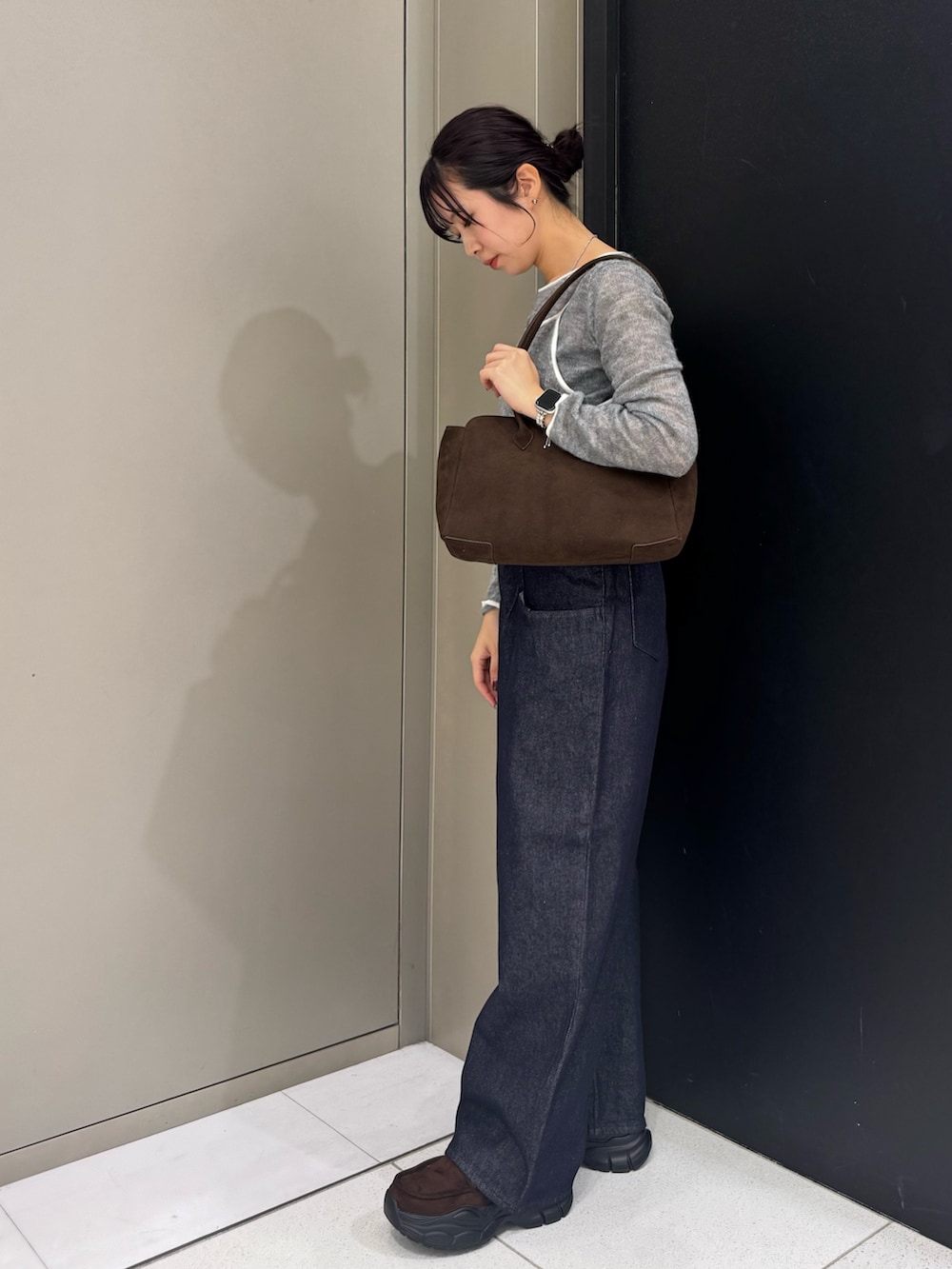 グレー系のニット/セーター、ブラウン系のボストンバッグ、ブルー系のデニムパンツを着用したレディースの秋コーディネートの2枚目の写真