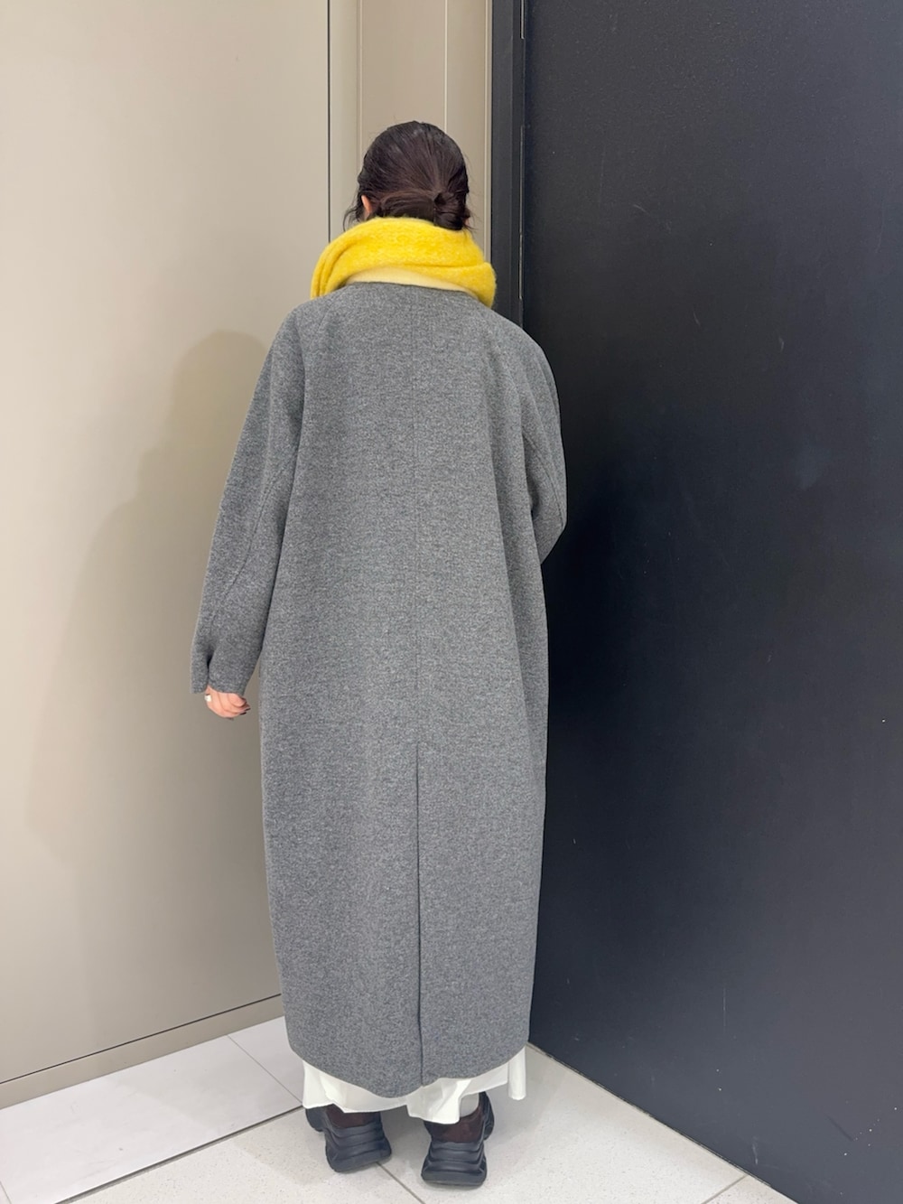 グレー系のステンカラーコート、ブラウン系のローファー、イエロー系のマフラーを着用したレディースの冬コーディネートの2枚目の写真