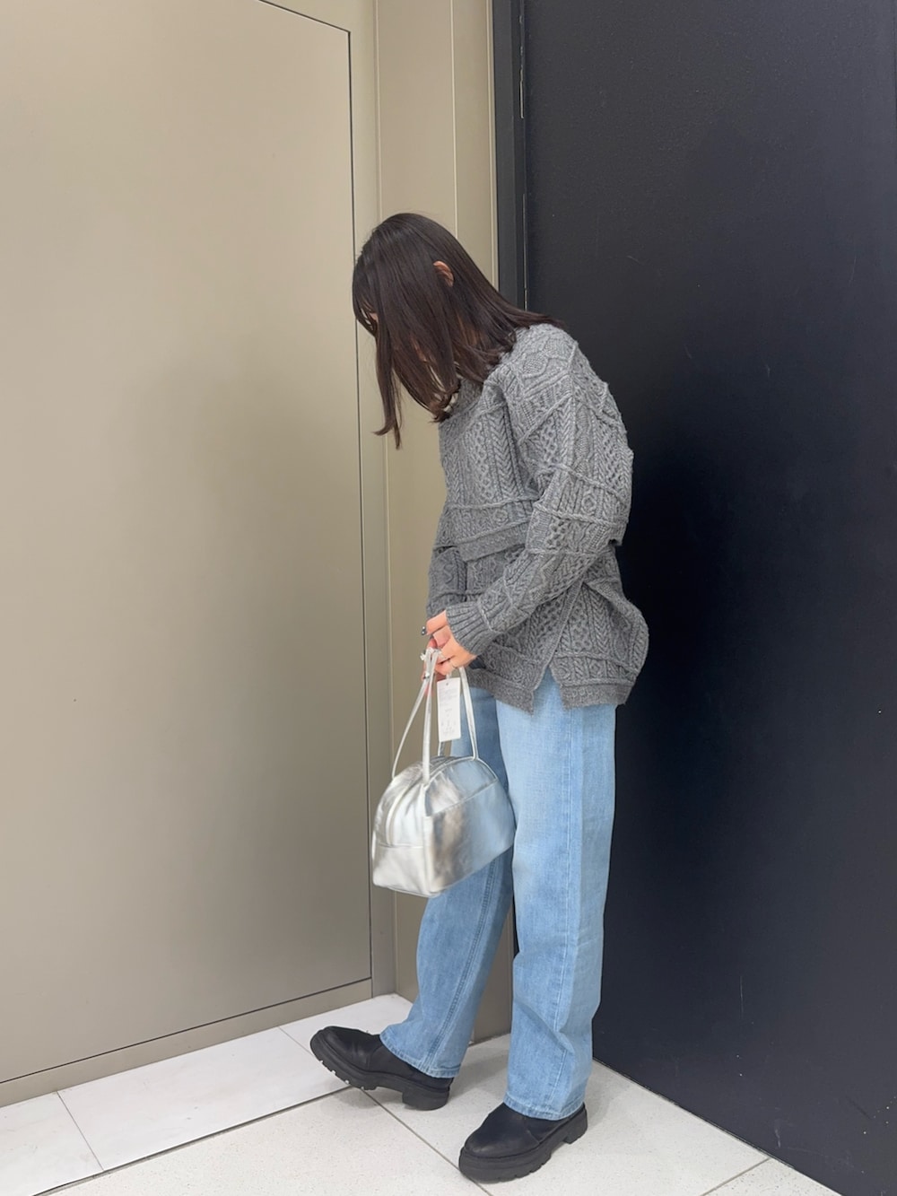 グレー系のニット/セーター、グレー系のスカート、シルバー系のボストンバッグを着用したレディースの冬コーディネートの2枚目の写真