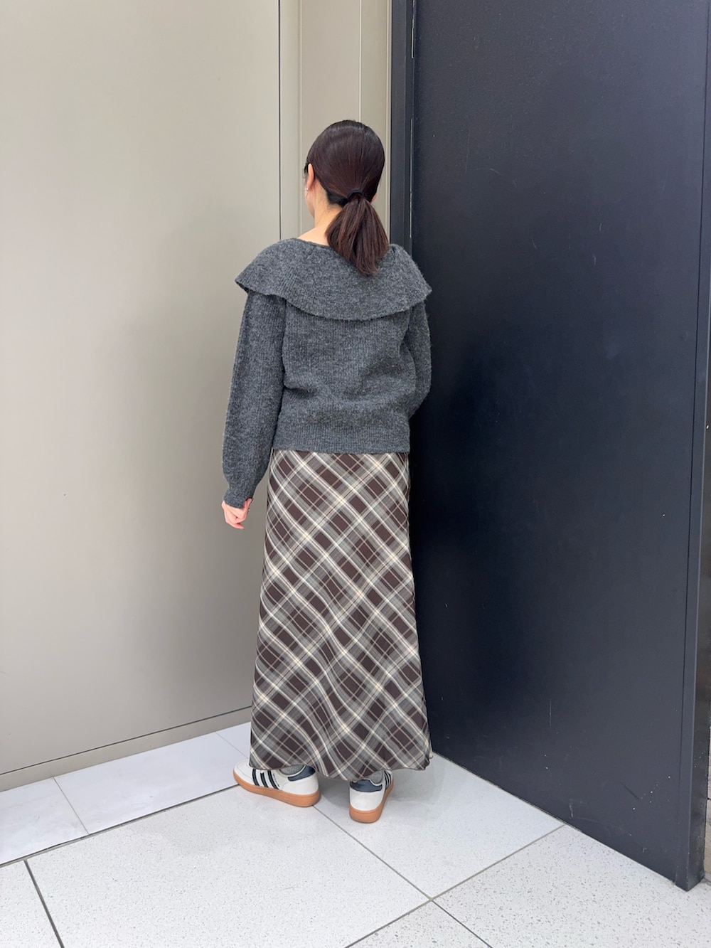 グレー系のニット/セーター、ブラック系のハンドバッグ、ブラウン系のスカートを着用したレディースの冬コーディネートの3枚目の写真