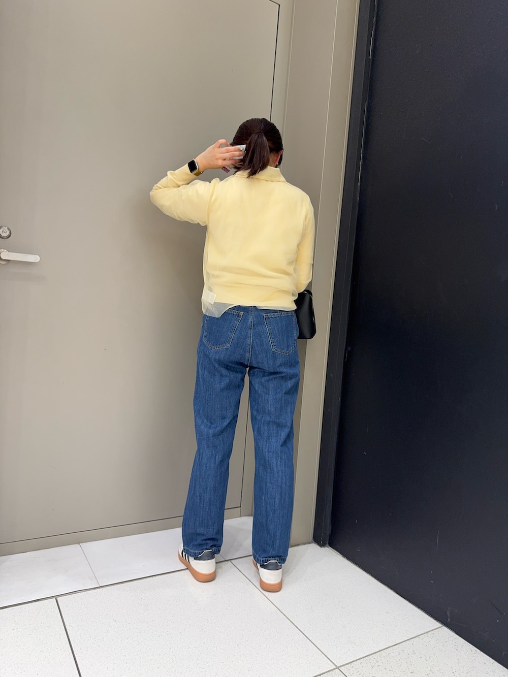 ブルー系のデニムパンツ、ホワイト系のニット/セーター、ブラック系のハンドバッグを着用したレディースの冬コーディネートの2枚目の写真