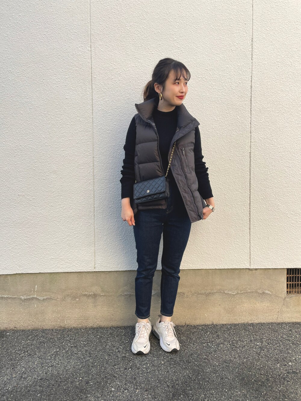 グレー系のダウンベスト、ベージュ系のスニーカー、ブラック系のニット/セーターを着用したレディースの秋コーディネートの2枚目の写真