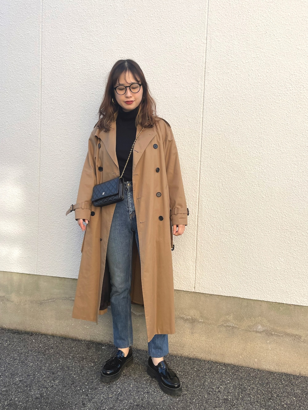 ブラック系のニット/セーター、ベージュ系のトレンチコート、ブルー系のデニムパンツを着用したレディースの秋コーディネートの2枚目の写真