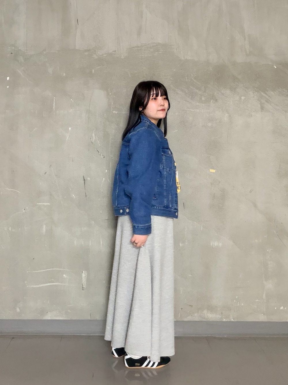 グレー系のスカート、イエロー系のTシャツ/カットソー、ブラック系のスニーカーを着用したレディースの春コーディネートの2枚目の写真