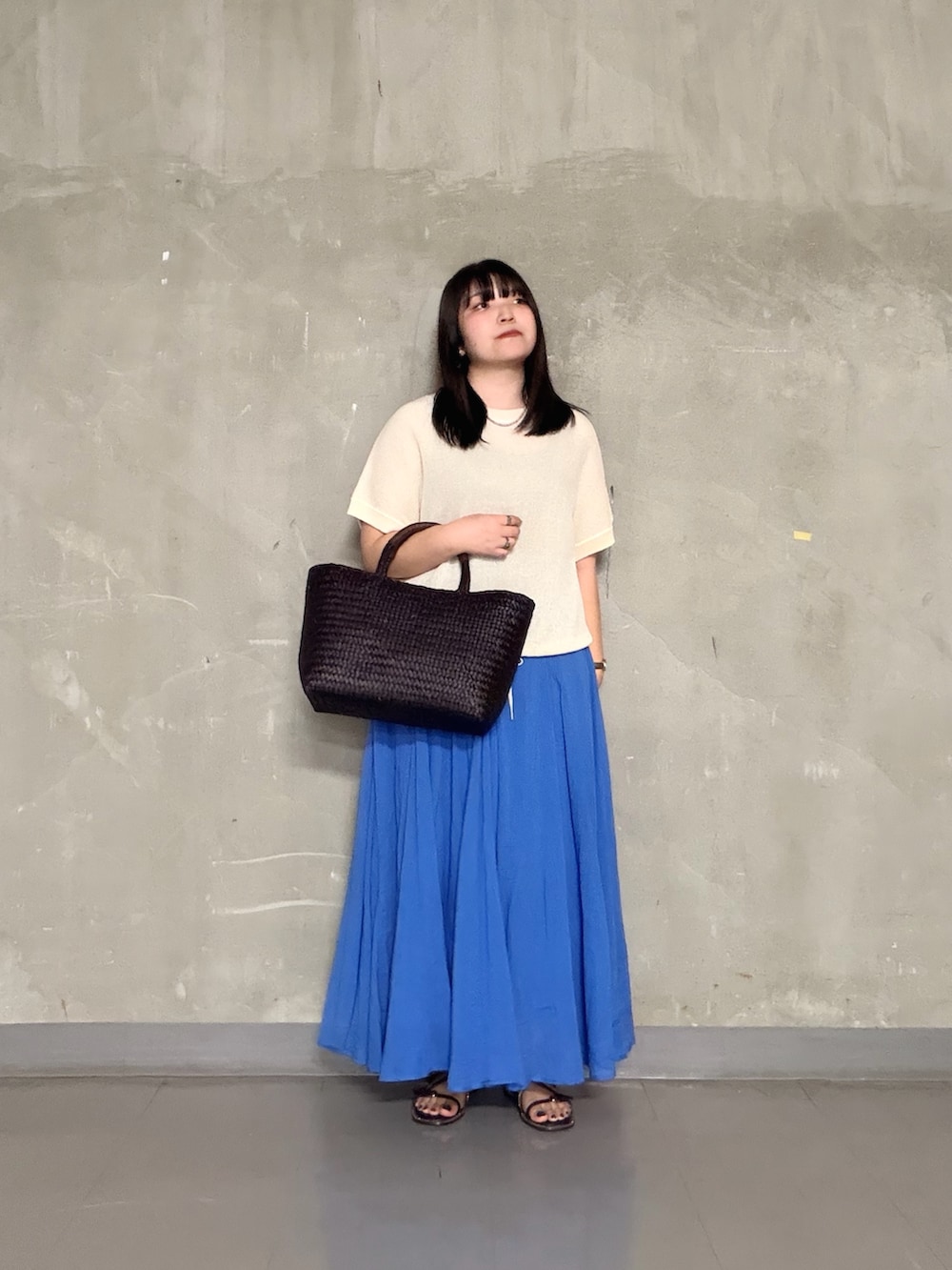 ブラウン系のトートバッグ、ホワイト系のニット/セーター、ブルー系のスカートを着用したレディースの夏コーディネートの4枚目の写真