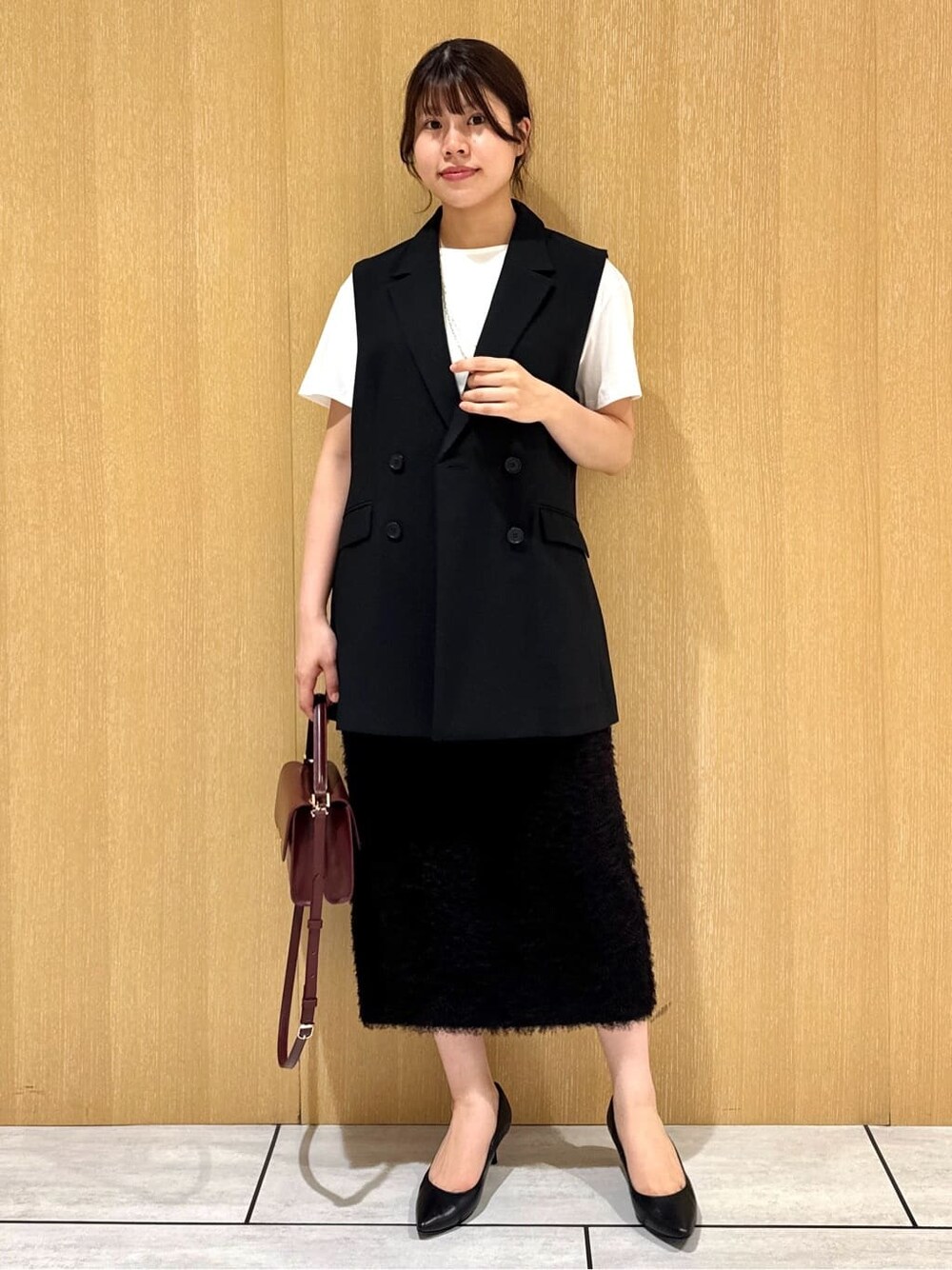ブラック系のベスト、ホワイト系のTシャツ/カットソー、ブラウン系のスカートを着用したレディースの夏コーディネートの6枚目の写真