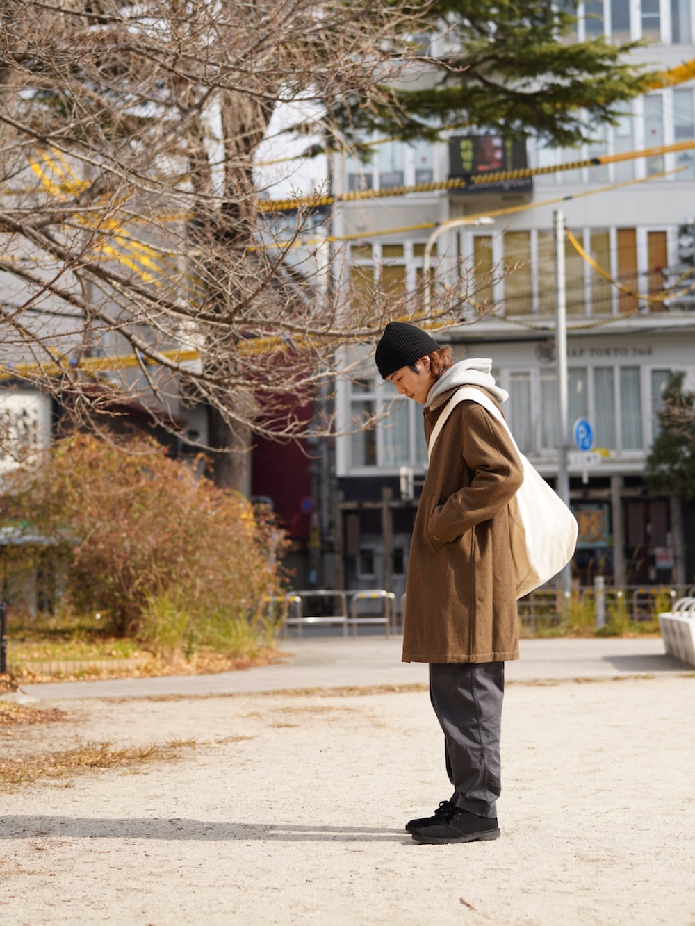 ブラウン系のステンカラーコート、グレー系のチノパンツ、ブラック系のブーツを着用したメンズの冬コーディネートの2枚目の写真