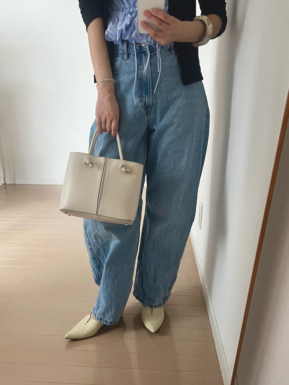 ブルー系のデニムパンツ、ホワイト系のパンプス、ブラック系のカーディガン/ボレロを着用したレディースの春コーディネートの2枚目の写真