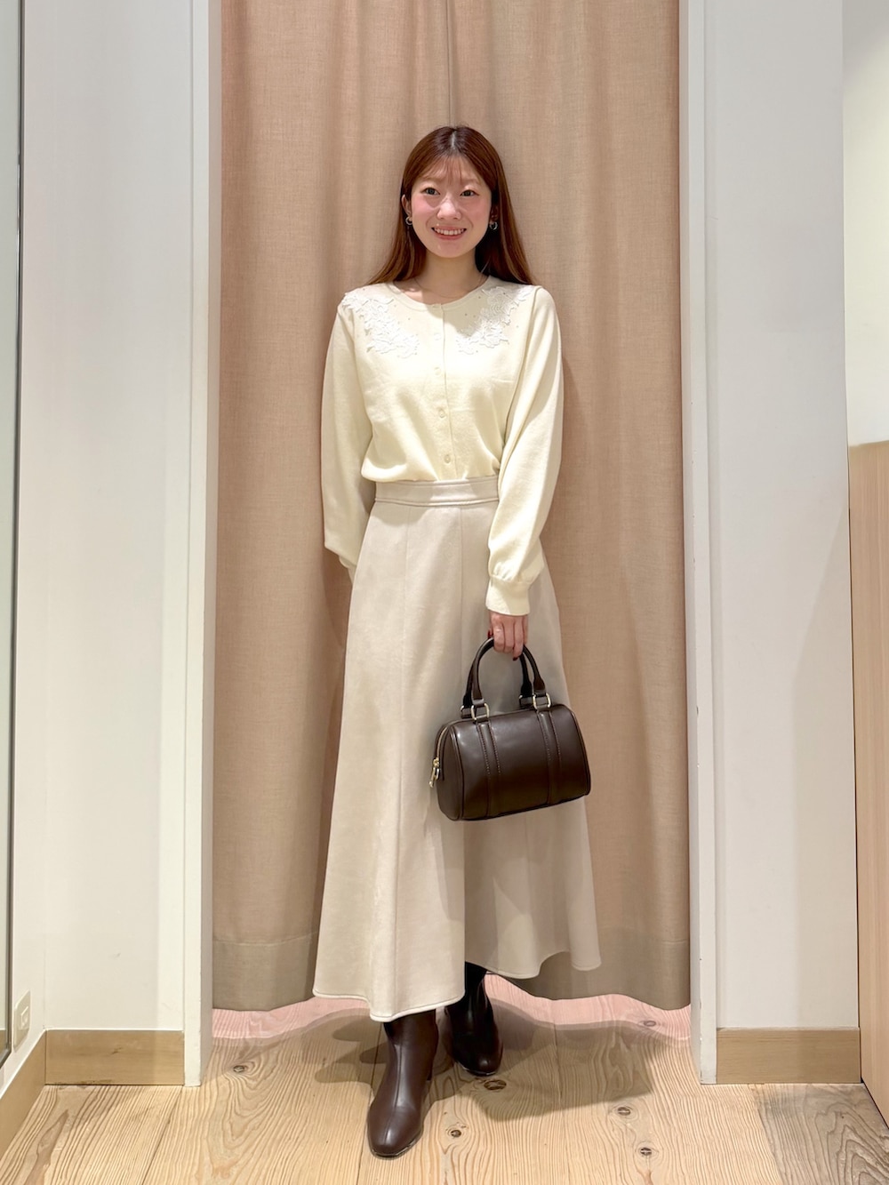 ホワイト系のカーディガン/ボレロ、ブラウン系のボストンバッグ、ベージュ系のスカートを着用したレディースの秋コーディネートの2枚目の写真