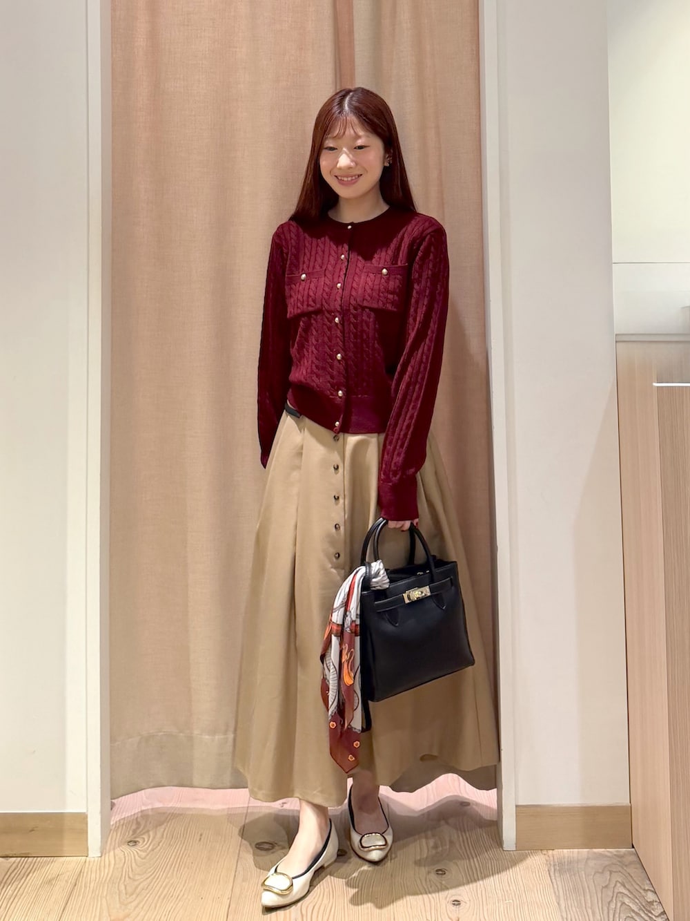 ベージュ系のスカート、ブラック系のトートバッグ、レッド系のアンサンブルを着用したレディースの秋コーディネートの3枚目の写真
