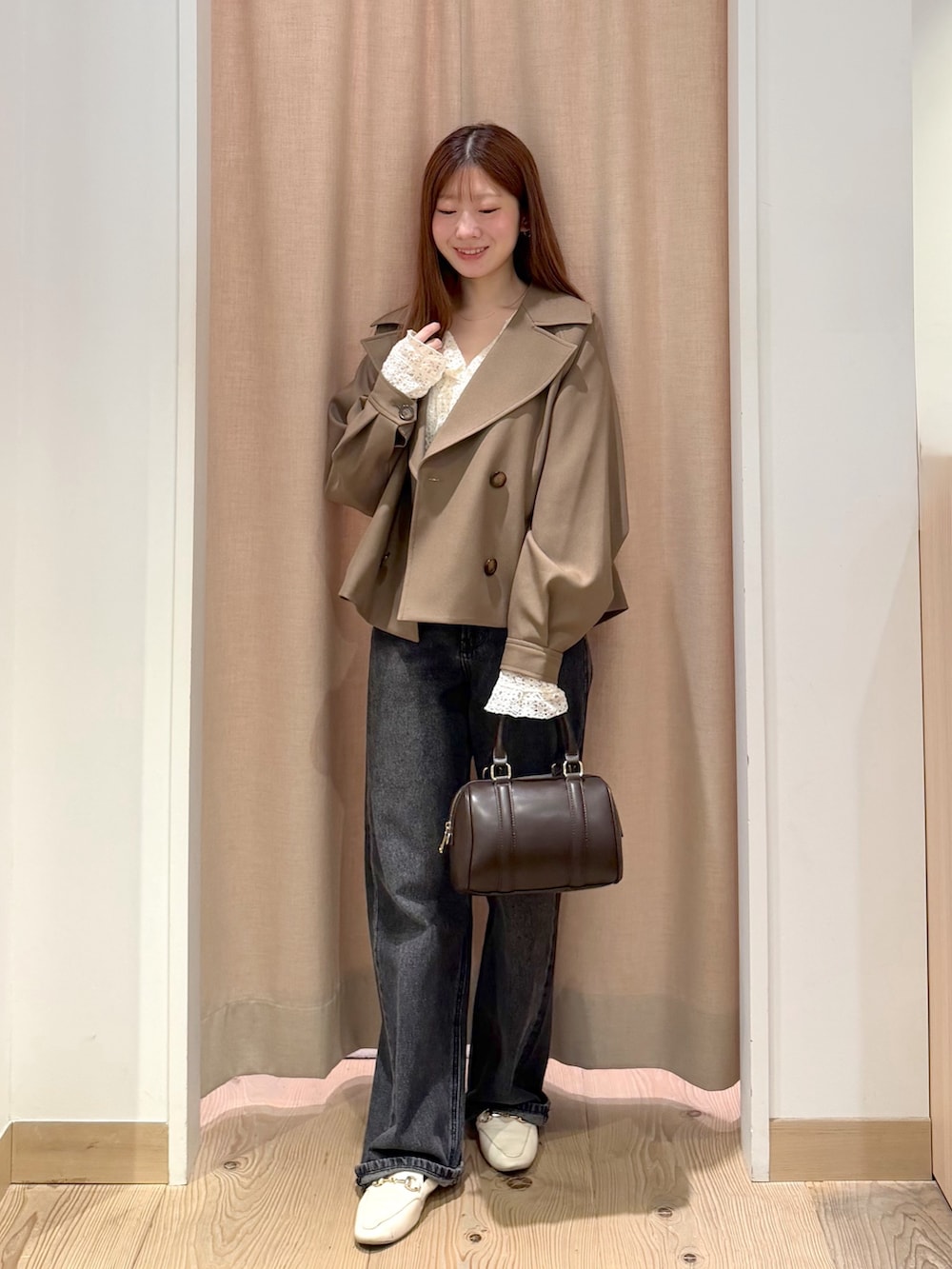 ブラック系のデニムパンツ、ブラウン系のボストンバッグ、ブラウン系のトレンチコートを着用したレディースの秋コーディネートの3枚目の写真