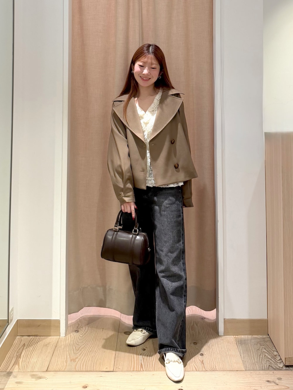 ブラック系のデニムパンツ、ブラウン系のボストンバッグ、ブラウン系のトレンチコートを着用したレディースの秋コーディネートの5枚目の写真