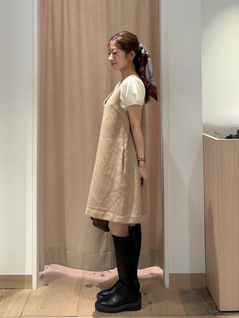 イエロー系のワンピース、ブラウン系のハンドバッグ、ブラック系のブーツを着用したレディースの秋コーディネートの3枚目の写真