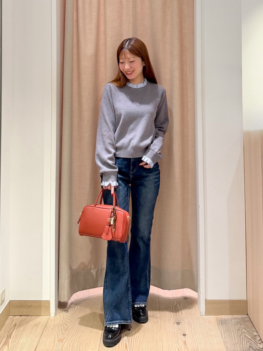 オレンジ系のボストンバッグ、ブルー系のデニムパンツ、グレー系のニット/セーターを着用したレディースの秋コーディネートの2枚目の写真